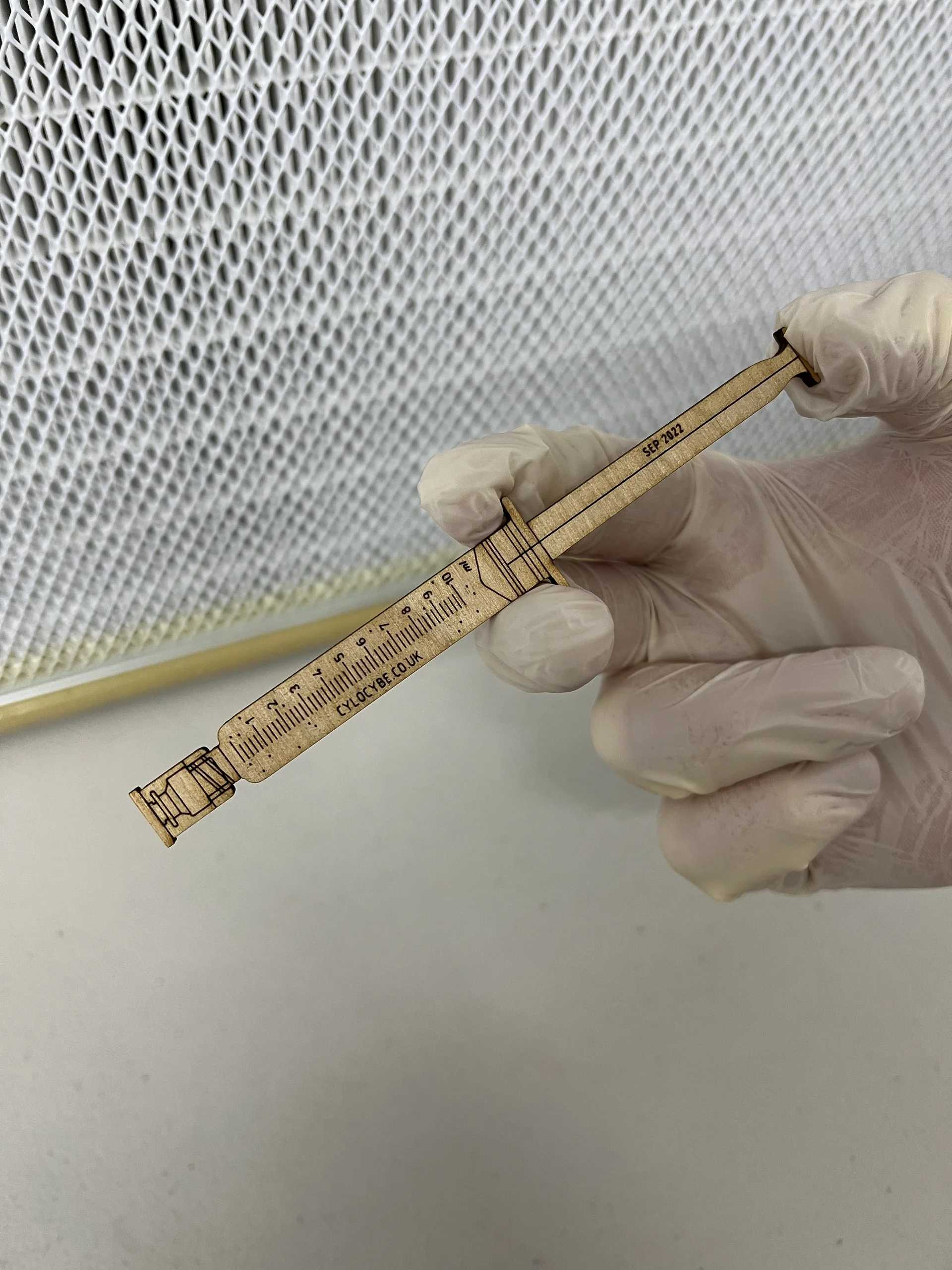 A laser-cut wooden Cylocybe syringe keepsake held in a gloved hand